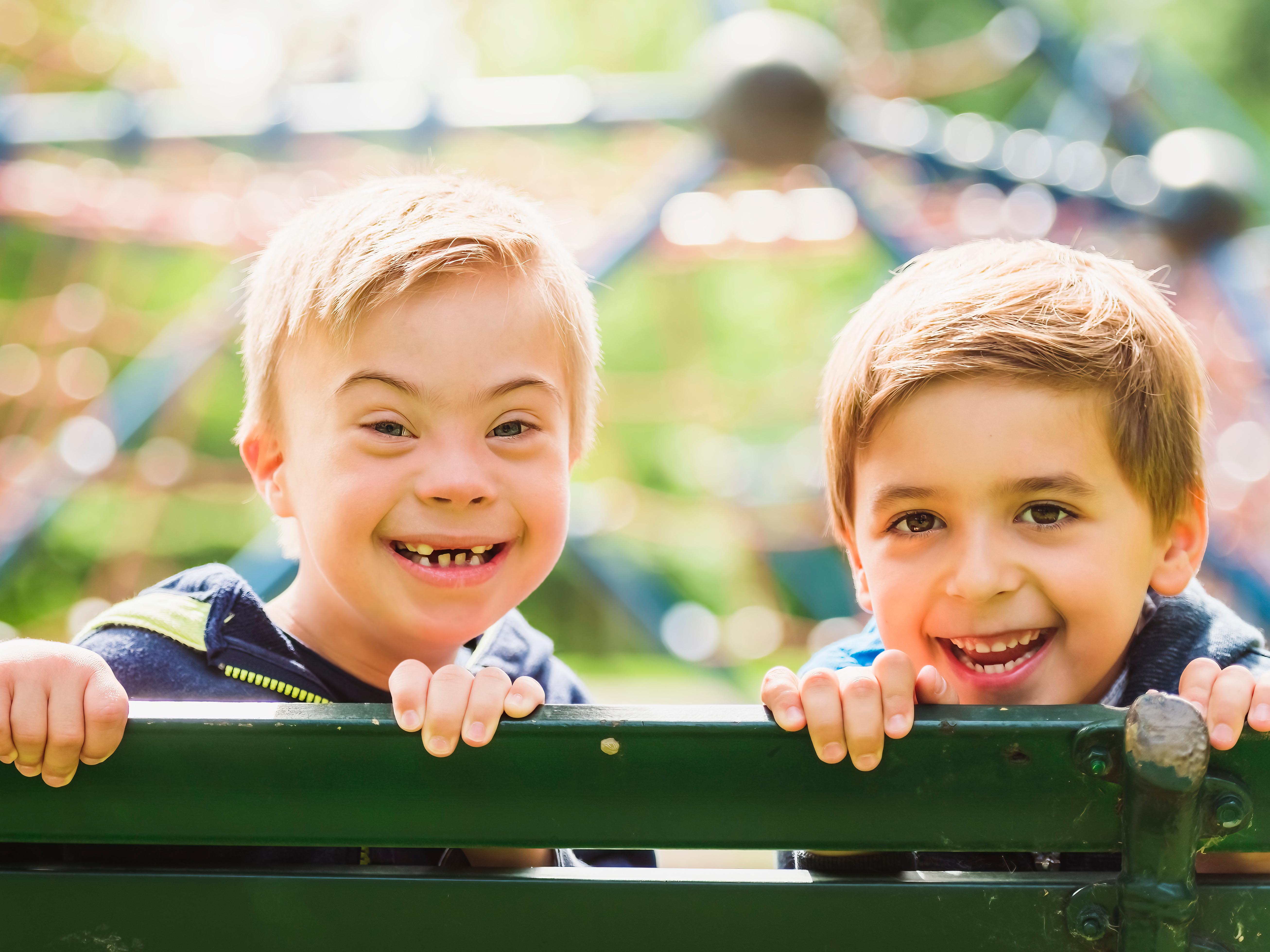 Portrait of a little boy with down syndrome sit on a bench with his brother
